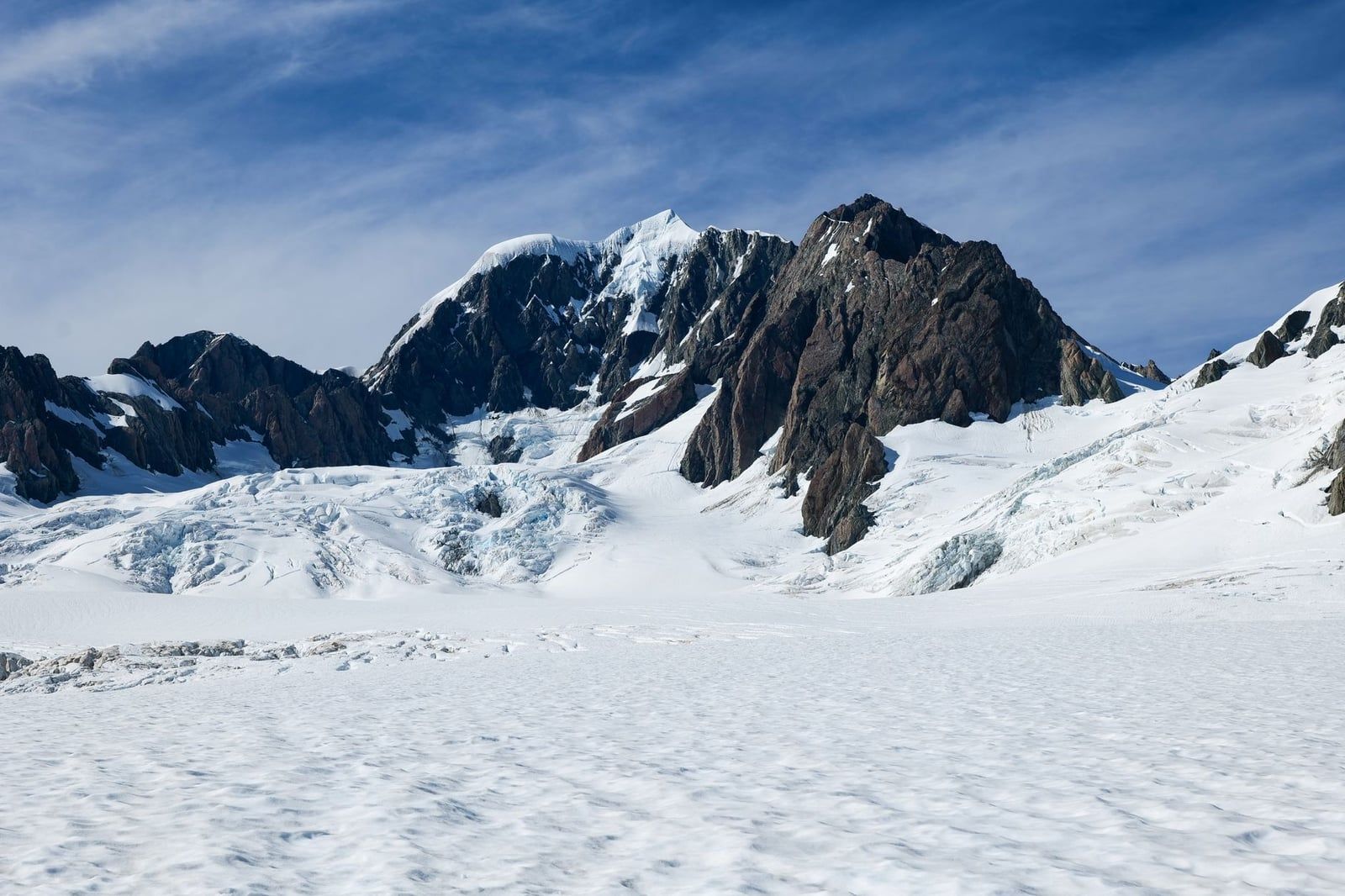 Nieve y hielo se extienden por el glaciar Fox hacia escarpados picos alpinos bajo un cielo azul.