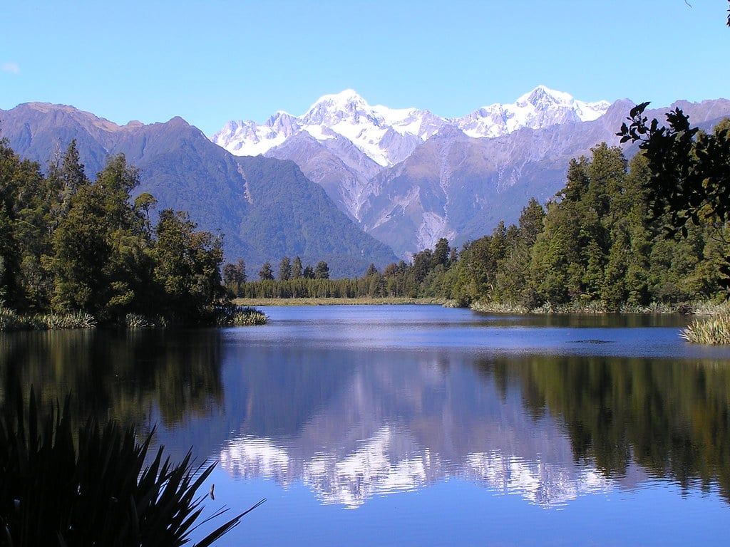 Snow-capped Southern Alps peaks reflect across the still surface of Lake Matheson near Franz Josef Glacier.